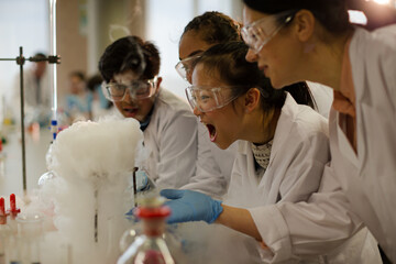 Female teacher and students watching scientific experiment chemical reaction in laboratory classroom