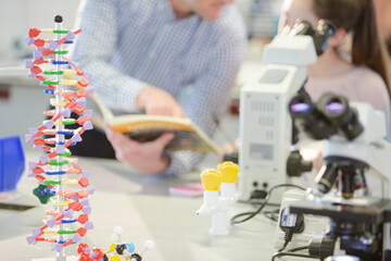 Male teacher helping girl student at microscope in laboratory classroom