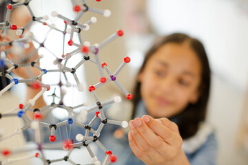 Curious girl student examining molecular structure in laboratory classroom