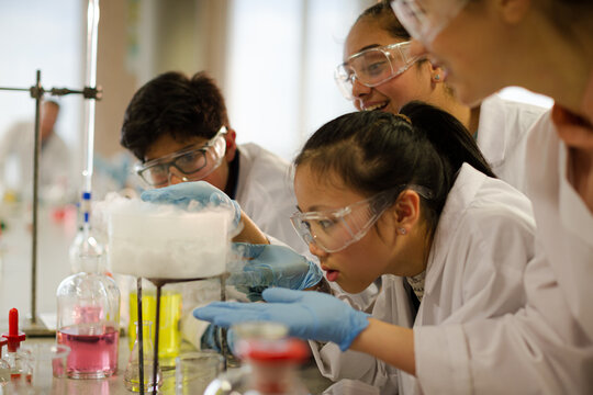 Female teacher and students watching scientific experiment chemical reaction in laboratory classroom