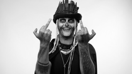 Sinister man with skull makeup making faces and showing middle finger. Bad manner gesture. Scary...