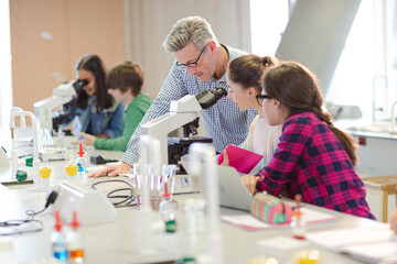 Obraz premium Male teacher helping girl students at microscope in laboratory classroom
