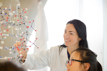 Female teacher and girl students examining molecular structure in classroom