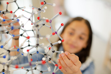 Curious girl student examining molecular structure in laboratory classroom