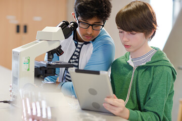 Focused boy students using digital tablet at microscope in laboratory classroom