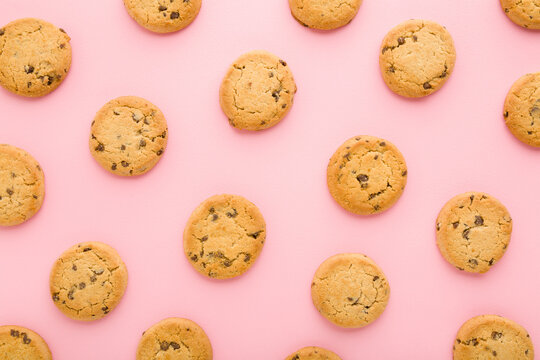 Dry cookies with chocolate pieces on light pink table background. Pastel color. Closeup. Sweet snacks. Biscuit pattern. Top down view.