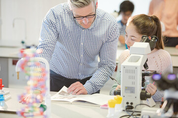 Male teacher helping girl student at microscope in laboratory classroom