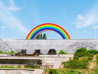 City street view with colorful rainbow on a sunny day with vibrant blue sky. LGBTQ pride concept. Park with gay rainbow symbol.