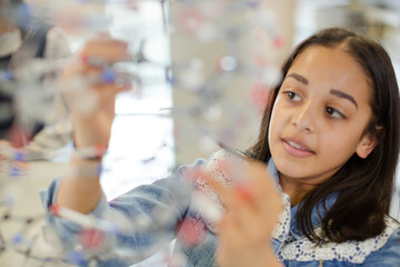 Curious girl student examining molecular structure in laboratory classroom