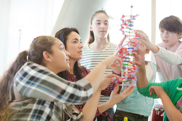 Female teacher and students examining DNA model in classroom