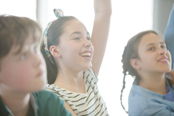 Eager, smiling students raising hands in classroom