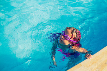 A girl in swimming glasses has fun and splashes in the pool.