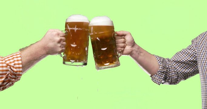 Celebration beer cheers concept - close up male hands holding glasses of beer at Oktoberfest traditional party or victory competition or successful task meeting. Isolated on green background