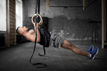 fitness, sport, bodybuilding and people concept - young man exercising on gymnastic rings in gym
