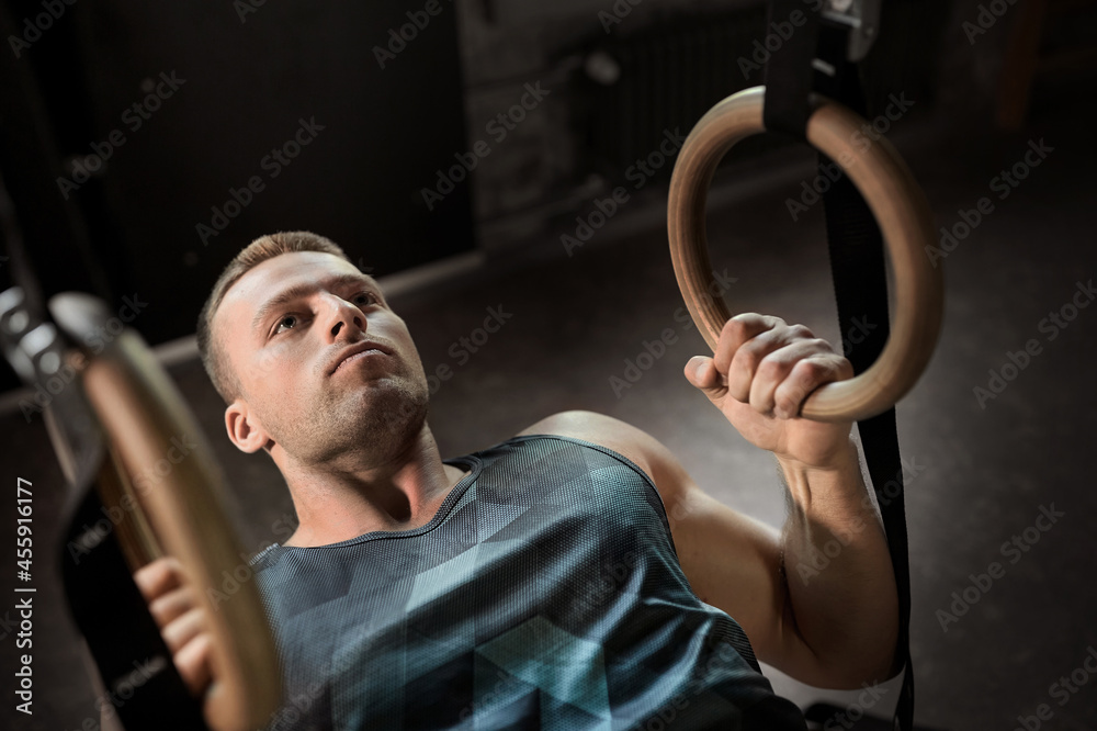 Poster fitness, sport, bodybuilding and people concept - young man exercising on gymnastic rings in gym