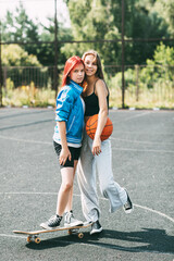 Portrait of two teenage girls with a basketball and a skateboard on a sports field