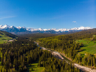 Top view of the beautiful green meadows and the Białka River, in the distance the snow-capped peaks of the Tatra Mountains. View from the air. View from the drone.