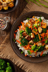 Tofu with rice and vegetables. Served on brown plate with chopsticks. Top view. - obrazy, fototapety, plakaty