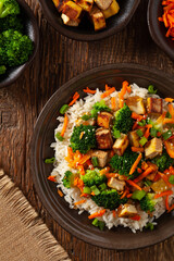 Tofu with rice and vegetables. Served on brown plate with chopsticks. Top view.