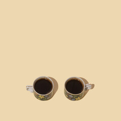 Two antique cups filled with fresh hot blend of black coffee. Arrangement made with copy space on beige background.