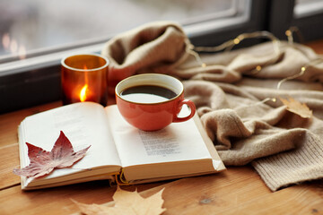 season, leisure and objects concept - cup of coffee, book, autumn leaves and candle on window sill at home