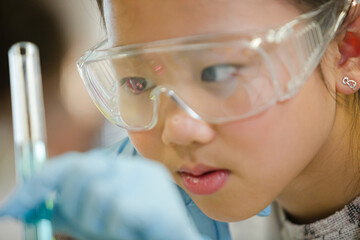 Girl students conducting scientific experiment, examining liquid in test tube in laboratory classroom