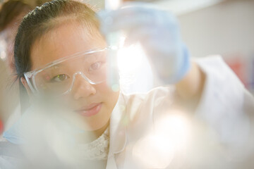 Girl students conducting scientific experiment, examining liquid in test tube in laboratory classroom