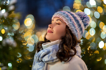 winter holidays and people concept - portrait of happy smiling young woman with closed eyes over christmas lights