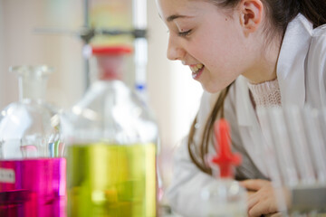 Girl student examining pink liquid, conducting scientific experiment in laboratory classroom