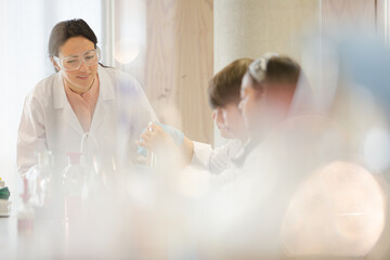 Female teacher and students conducting scientific experiment, watching liquid in test tube in laboratory classroom
