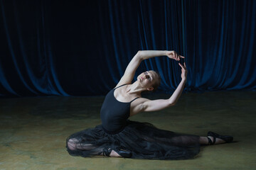 A ballerina in a black ballet costume rehearses on stage.