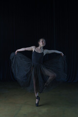 A ballerina in a black ballet costume rehearses on stage.