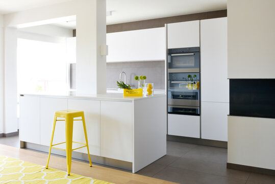 Luminous white kitchen with grey walls, yellow furnitures, and two ovens