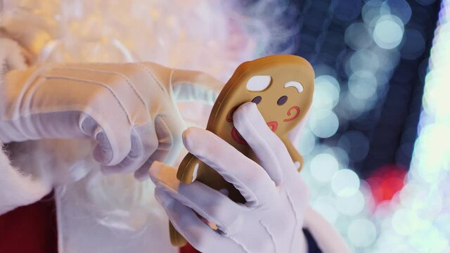 Close-up of hands, Santa Claus uses a smartphone in a case in the form of cookies on the background of blinking Christmas garlands