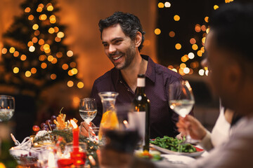 holidays, party and celebration concept - multiethnic group of happy friends having christmas dinner at home and drinking wine