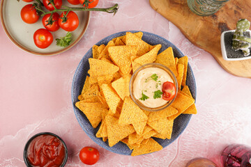 A blue bowl with cheese tortilla chips and a chilli cheese dip on a pink marble surface, cherry tomatoes, ketchup, top view