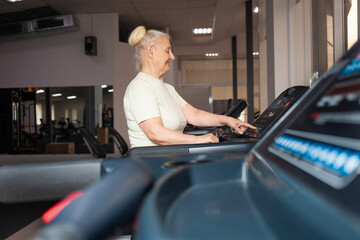 eldest woman of retirement age runs on a treadmill in the gym. Happy, smiling, portrait. Active, athletic, healthy lifestyle in old age. Concept senior. Modern technologies. indoors