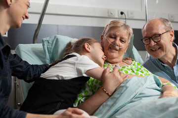 Family visiting sick retired senior woman in hospital ward during clinical therapy. Caring...