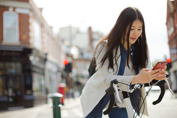 Fototapeta na wymiar Young woman commuting on bicycle, texting with cell phone on sunny urban street
