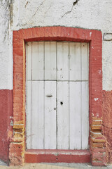 Worn and unpainted red with white facade with a white painted wooden door with copy space