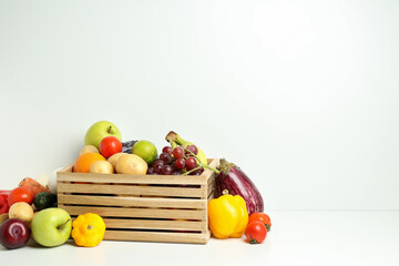 Wooden box with different vegetables and fruits on white table
