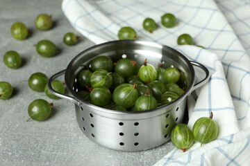 Pot of ripe gooseberry and kitchen towel on gray textured table