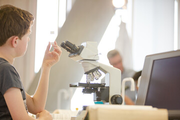 Boy student conducting scientific experiment at microscope and computer in laboratory classroom