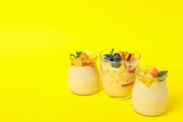 Glass jars with peach yogurt on yellow background