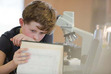 Boy student conducting scientific experiment at microscope and computer in laboratory classroom