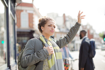 Smiling young woman hailing taxi on sunny urban street