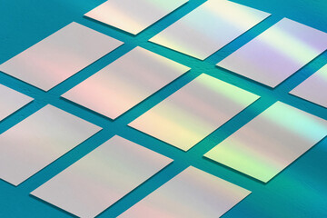 Many empty white horizontal rectangle a4 poster, business card or flyer mockups lying diagonally with overlay of rainbow light refraction caustic effect on blue concrete background. Isometric view