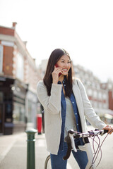 Smiling young woman commuting on bicycle, talking on cell phone on sunny urban street