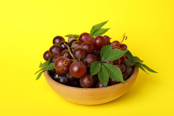 Bowl ripe grape on yellow background, close up