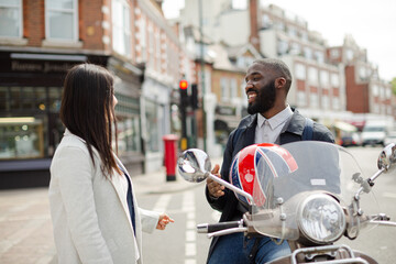 Affectionate young couple talking at motor scooter on sunny urban street